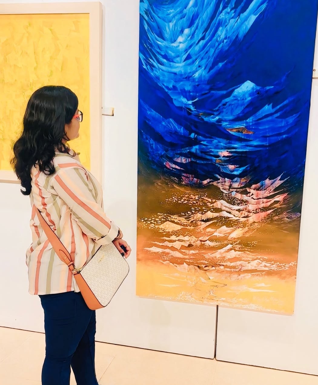 Nisha, founder of Nisha Arts, viewing a large abstract blue and gold painting in an art gallery